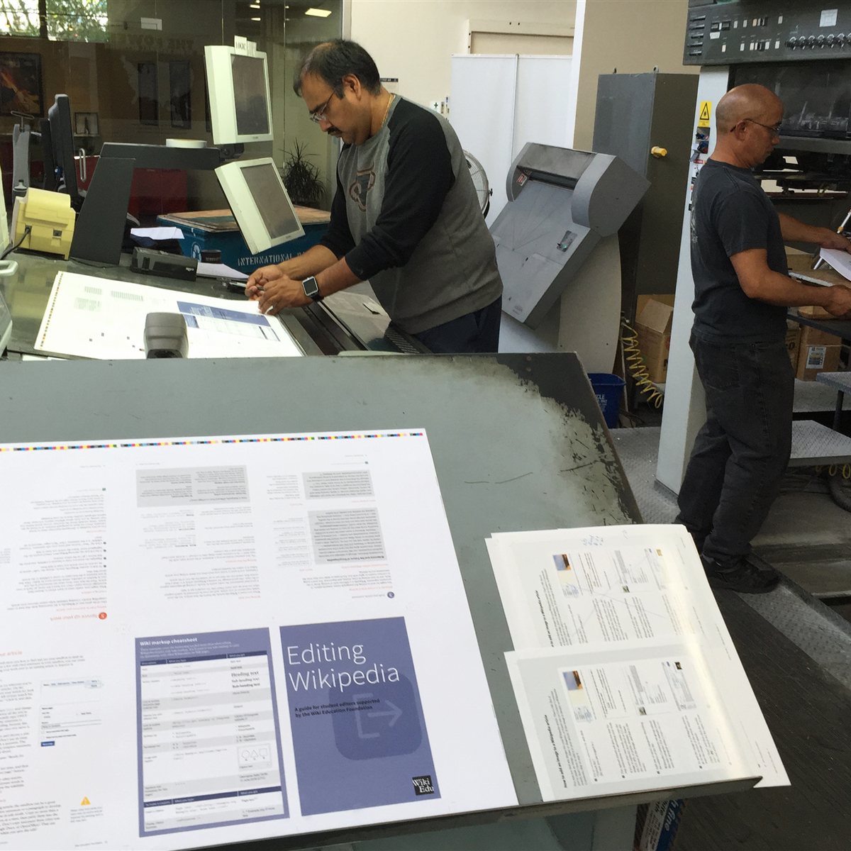 Illustrative photo of an offset-press check: workers examine printed sheets; not a photograph of Gràfiques Manlleu
