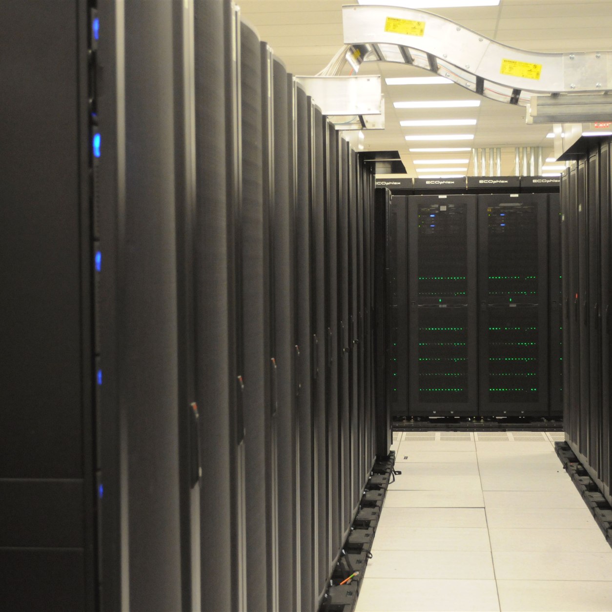 Photograph of rows of server racks at NERSC with overhead cable trays, illustrating local AI server siting